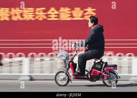 PEKING – ÜLG. 25, 2011. Mann auf dem Elektrofahrrad in Peking. Viele Einwohner von Peking kaufen batteriebetriebene Zweirad-Fahrräder, um Stau zu vermeiden. Stockfoto