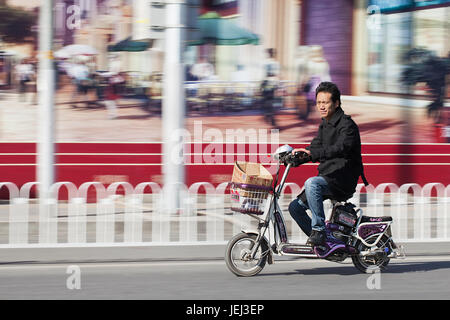 PEKING – ÜLG. 25, 2011. Mann auf dem Elektrofahrrad in Peking. Viele Einwohner von Peking kaufen batteriebetriebene Zweirad-Fahrräder, um Stau zu vermeiden. Stockfoto