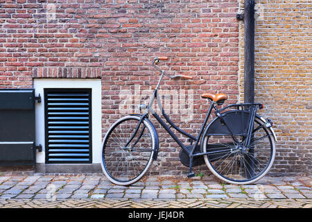 Schwarzes klassisches Fahrrad geparkt vor einer roten Backsteinmauer, Amsterdam, Niederlande Stockfoto