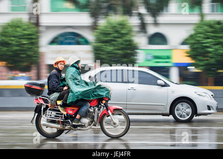 GUANGZHOU-FEB. 25, 2012. Motorrad-Taxi im Regen mit Passagier mit städtischen Szene in Bewegung Unschärfe auf dem Hintergrund. Stockfoto