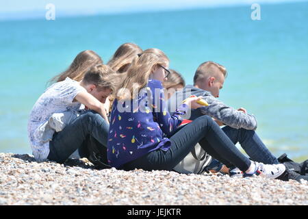Gruppe von jungen Studenten sitzen auf einem Kiesstrand an einem heißen Tag im Sommer in Großbritannien. Stockfoto