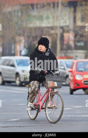 PEKING - 4. DEZEMBER 2012. Winter kleidete Frau auf einem Fahrrad. 2015 kämpfte China mit einer rekordbrechenden starken Kaltwelle von Nord nach Süd. Stockfoto