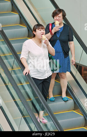 PEKING - 19. AUGUST 2015. Fette Frau isst Eis auf Rolltreppe. Die chinesische Fettleibigkeitsrate ist in den letzten drei Jahrzehnten in die Höhe geschossen. Stockfoto