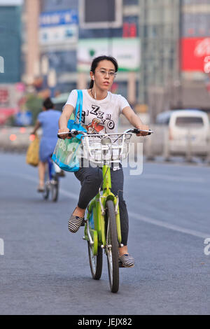 PEKING - 10. JULI 2015. Junge Frau fährt mit einem öffentlichen Fahrrad. Fahrradnutzung ermöglicht die kurzfristige Anmietung, es ist ein sehr beliebter Transportmodus. Stockfoto