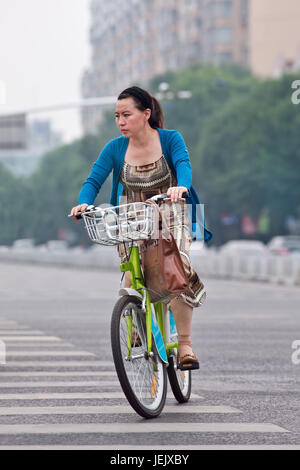 PEKING - 27. JULI 2015. Elegante Frau auf einem öffentlichen Fahrrad. Fahrradnutzung ermöglicht die kurzfristige Anmietung, es ist ein sehr beliebter Transportmodus. Stockfoto