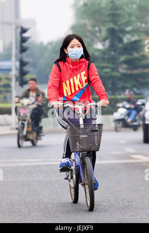 PEKING-OCT. 19, 2014. Maskierter Radfahrer in rauchiger Stadt. Peking erhöhte Smog auf Orange, weil die schlechte Luftqualität. Stockfoto