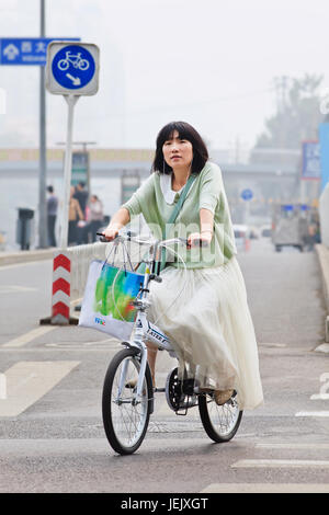 PEKING - 6. OKTOBER 2013. Mädchen auf EINEM klappbaren Fahrrad im smog verblondete Innenstadt. Stockfoto