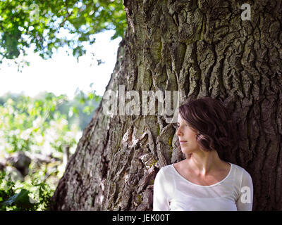 Junge Frau, die wegsehen, Alter Baum im Hintergrund Stockfoto