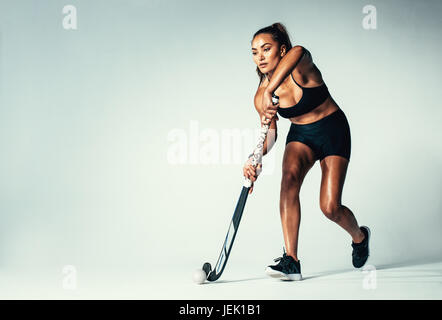 Voller Länge des Frau-Eishockey-Spieler dribbeln Ball auf grauem Hintergrund. Hispanische Frauen Hockey im Studio zu spielen. Stockfoto