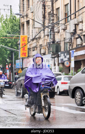 Chinesischer Mann in Regenbekleidung gekleidet mit dem e-Bike. Shanghai hat einen feuchten subtropischen Klimas, der Sommer ist sehr warm und schwül. Stockfoto