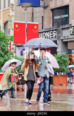 Shopper mit Regenschirm in den nassen Nanjing East Road. Shanghai hat einen feuchten subtropischen Klimas, der Sommer ist sehr warm und schwül. Stockfoto