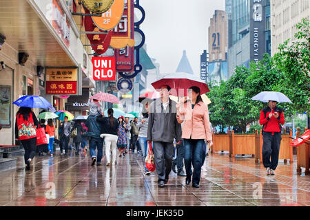 Shopper mit Regenschirm in den nassen Nanjing East Road. Shanghai hat einen feuchten subtropischen Klimas, der Sommer ist sehr warm und schwül. Stockfoto