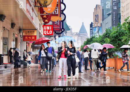 Shopper mit Regenschirm in den nassen Nanjing East Road. Shanghai hat einen feuchten subtropischen Klimas, der Sommer ist sehr warm und schwül. Stockfoto