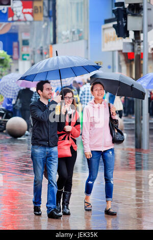 Kaukasische Paar und Chinesische Mädchen mit Regenschirm im Stadtzentrum. Shanghai hat feuchten subtropischen Klima, der Sommer ist warm und feucht. Stockfoto