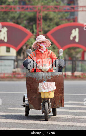 PEKING, 9. JUNI 2015. Weibliche Kehrmaschine mit Mundkappe auf elektrischem Trike. Dank einer Armee von Straßenfeger Peking Stadtzentrum ist sehr sauber. Stockfoto