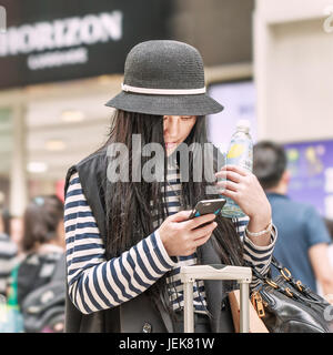 PEKING-21. MAI 2016. Modische junge chinesische Mädchen beschäftigt mit Smartphone in einem belebten Einkaufszentrum. Stockfoto