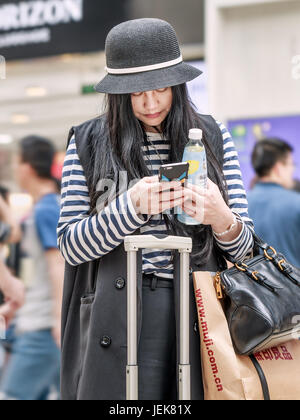 PEKING-21. MAI 2016. Modisch gekleidet chinesischen jungen Mädchen beschäftigt mit ihrem Smartphone in einem Einkaufszentrum. Stockfoto