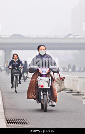 PEKING-OCT. 11,2014. Frau auf E-Bike in der Stadt mit Smog-Decke. Eine Konzentration von PM2.5, kleinen Partikeln, die ein großes Gesundheitsrisiko darstellen. Stockfoto