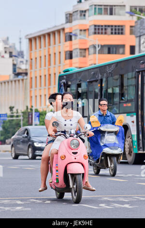 KUNMING - 30. JUNI 2014. Mädchen mit Mundkappe auf E-Bike. Immer mehr chinesische Bürger tragen Atemschutz vor Luftverschmutzung. Stockfoto
