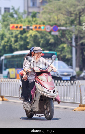 KUNMING - 5. JULI 2014. Fröhliche Frau auf dem Elektro-Rad. Viele Elektrofahrräder in China sind das E-Bike im Roller-Stil, das Pedale haben kann oder nicht. Stockfoto