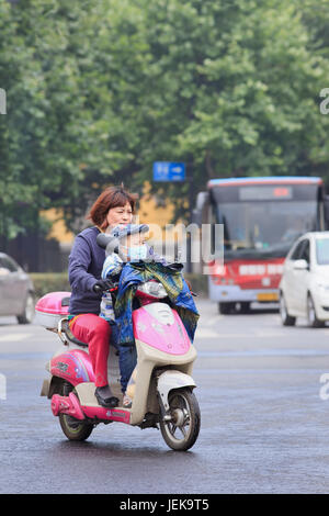 NANJING - 25. MAI 2014. Frau auf E-Bike mit Kind, das Atemschutz trägt. Immer mehr Chinesen tragen Atemschutz vor Verschmutzung. Stockfoto