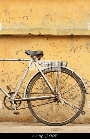 Rostiges chinesisches Fahrrad gegen den verwitterten gelben Wallstandard Stockfoto