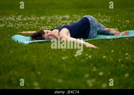 Schöne Caucaisan junge Frau im Freien auf der blauen Matte trainieren. Jathara Parivartanasana Draufsicht Stockfoto