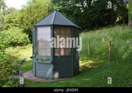 Achteckige lackiertem Holz Holz Sommerhaus Sommerhaus in Rasen und Garten mit Drahtgitter bestand Rinder Zaun und Wald im Hintergrund UK Stockfoto