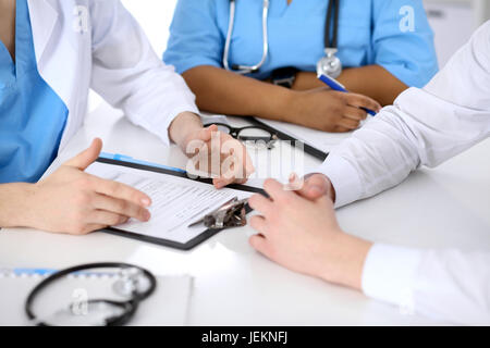 Zwei Ärzte und männlicher Patient diskutieren Krankengeschichte am Tisch, Nahaufnahme Stockfoto