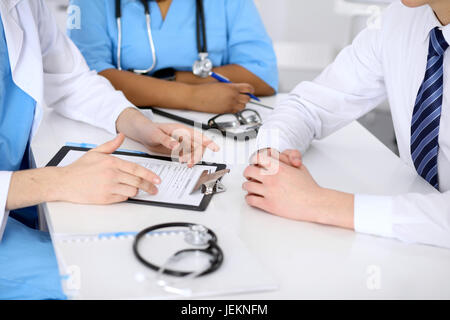 Zwei Ärzte und männlicher Patient diskutieren Krankengeschichte am Tisch, Nahaufnahme Stockfoto