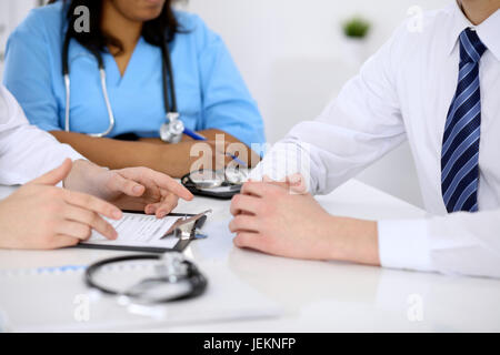 Zwei Ärzte und männlicher Patient diskutieren Krankengeschichte am Tisch, Nahaufnahme Stockfoto