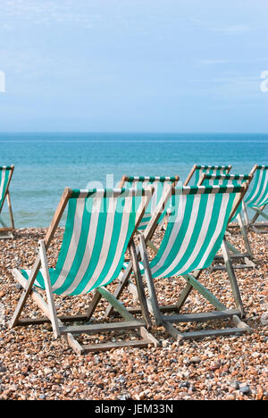 Sieben leere Aqua grüne-weiße gestreifte Liegestühlen mit Blick aufs Meer auf einem Kiesstrand.  Heller, sonniger Tag mit Ble Sky. Stockfoto