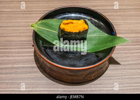 Uni-Sushi, Seeigel japanisches Essen in schwarze Platte und Blatt auf Holztisch Stockfoto