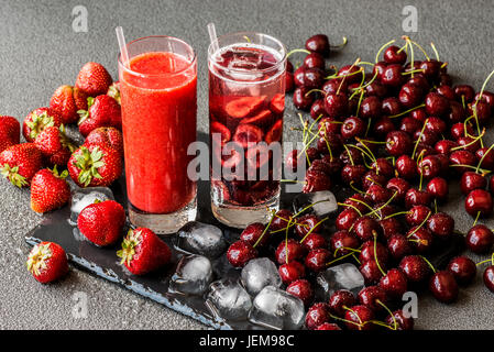 Frische Erdbeer Smoothie und Detox Wasser mit Kirschen in zwei Gläser auf einem grauen Hintergrund. Gesunde Entgiftung Getränke. Stockfoto