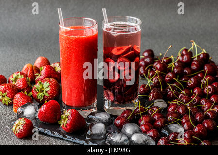 Frische Erdbeer Smoothie und Detox Wasser mit Kirschen in zwei Gläser auf einem grauen Hintergrund. Gesunde Entgiftung Getränke. Stockfoto