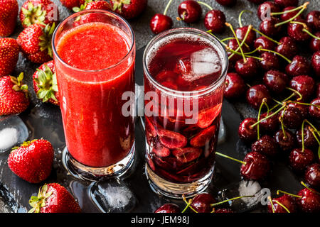 Frische Erdbeer Smoothie und Detox Wasser mit Kirschen in zwei Gläser auf einem grauen Hintergrund. Gesunde Entgiftung Getränke. Stockfoto