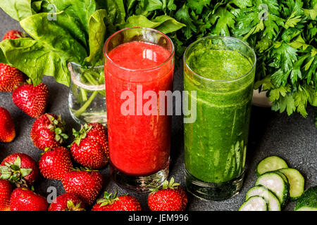 Erdbeer Smoothie und grünen Smoothie in zwei Gläser mit Zutaten auf einem grauen Hintergrund. Detox-gesunde Getränke. Stockfoto