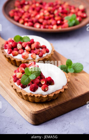 Wilde Erdbeeren Törtchen mit Creme füllen, köstliche Sommer Mini Obstkuchen auf rustikalen Schneidebrett Stockfoto
