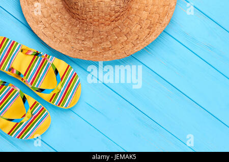 Teil des gewebten Hut, Sandalen. Nahaufnahme von Stroh Kopfbedeckungen und Flip-flops, hölzernen Hintergrund blau. Stockfoto