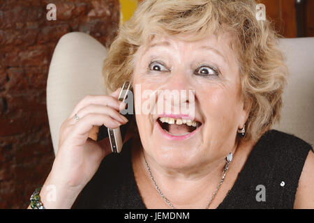 Porträt einer alten Frau am Telefon zu sprechen und auf Couch sitzen. Im Innenbereich. Stockfoto