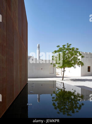 Blick in Richtung Moschee über Brunnen mit Corten-Wand. Gästehaus, Doha, Katar. Architekt: John McAslan und Partner, 2016. Stockfoto