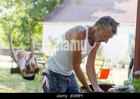 Mann im Garten, Mädchen schwingen auf Hintergrund Stockfoto