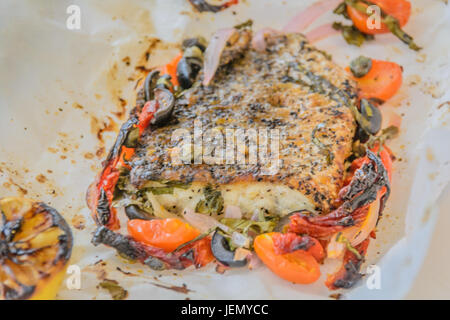 Al Cartoccio frischer Seebarsch Wolfsbarschfilet gekocht in Pergamentpapier mit sonnengetrockneten Tomaten, Sardellen und Kapern Stockfoto