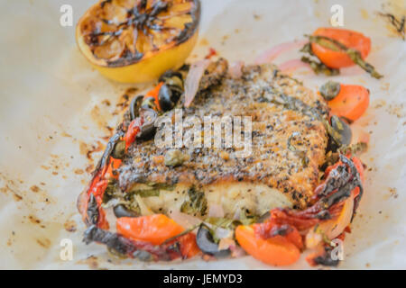 Al Cartoccio frischer Seebarsch Wolfsbarschfilet gekocht in Pergamentpapier mit sonnengetrockneten Tomaten, Sardellen und Kapern Stockfoto