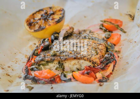 Al Cartoccio frischer Seebarsch Wolfsbarschfilet gekocht in Pergamentpapier mit sonnengetrockneten Tomaten, Sardellen und Kapern Stockfoto