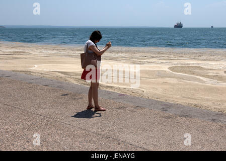 Thessaloniki, Griechenland. 27. Juni 2017. Eine Frau nimmt ein Bild der rote Flut betroffenen Küste der nördlichen Hafen der griechischen Stadt Thessaloniki. Red Tide ist eine gebräuchliche Bezeichnung für ein Phänomen bekannt als eine Algenblüte, verursacht durch Arten der Dinoflagellaten, die auf eine rote oder braune Farbe. Kredit Kredit: Orhan Zolak/Alamy Live-Nachrichten Stockfoto