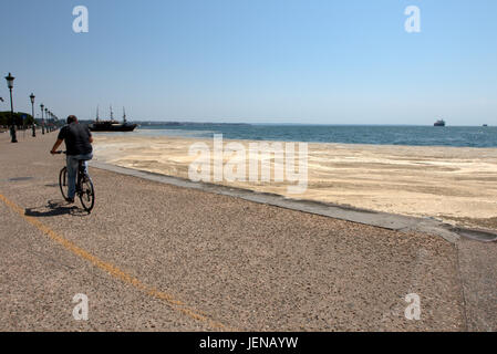 Thessaloniki, Griechenland. 27. Juni 2017. Ein Radfahrer fährt Vergangenheit die rote Flut Strandpromenade von der nördlichen griechischen Hafen von Thessaloniki betroffen. Red Tide ist eine gebräuchliche Bezeichnung für ein Phänomen bekannt als eine Algenblüte, verursacht durch Arten der Dinoflagellaten, die auf eine rote oder braune Farbe. Kredit Kredit: Orhan Zolak/Alamy Live-Nachrichten Stockfoto