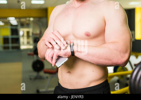 Nahaufnahme der sportlichen Mann nach Trainingseinheit Fitness Ergebnisse Smartphone überprüft. Erwachsener Mann trägt Sport Tracker Armband Arms Training hart innen Stockfoto