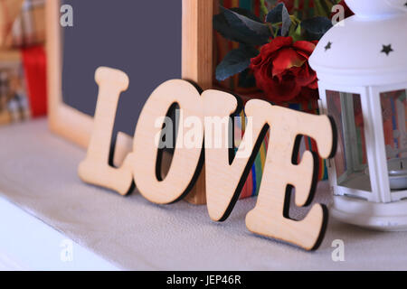 Das Wort Liebe, Tafel, Geschenkboxen, Rahmen und Laterne stehen auf dem Kamin. Stockfoto