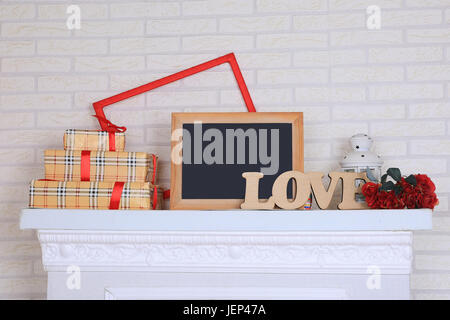 Das Wort Liebe, Tafel, Geschenkboxen, Rahmen und Laterne stehen auf dem Kamin. Stockfoto